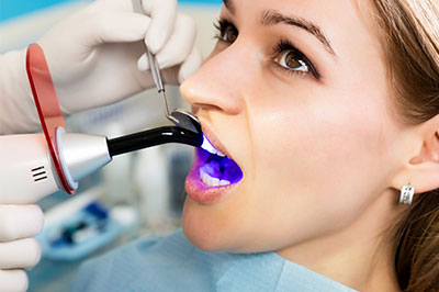 A woman receiving dental treatment with a dental device, surrounded by medical equipment, while wearing a surgical mask.