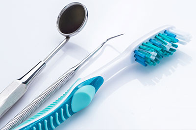 The image displays dental instruments, including a toothbrush with blue bristles, placed next to each other on a white surface.