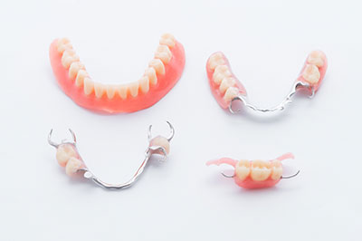 The image displays a collection of dental appliances including dentures with teeth and gum bases, and a pair of clear aligners typically used for orthodontic treatment.