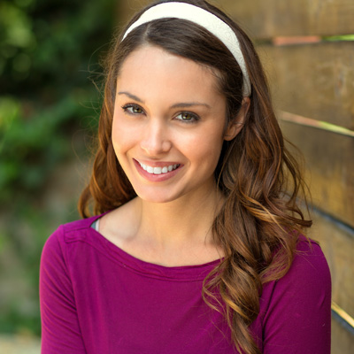 A woman with long hair wearing a purple top, smiling at the camera, posing for a portrait.