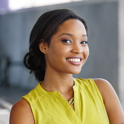 The image shows a woman with a radiant smile, wearing a yellow blouse, standing against a gray background.