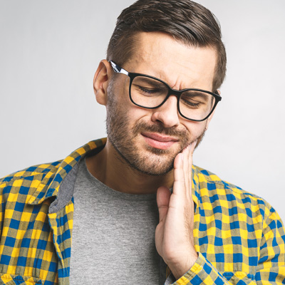 The image shows a man with glasses wearing a yellow plaid shirt, looking upwards with his hand on his chin, possibly indicating concern or contemplation.