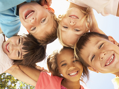 A group of children, both boys and girls, smiling together under the sun with their arms around each other s shoulders.