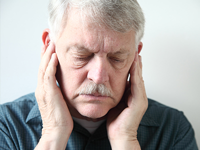 The image shows an older man with his hand on his face, appearing to be in pain or discomfort, with a pained expression.